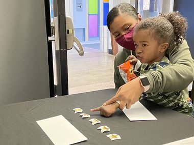 A dark haired woman and her child are at a black table. They are pointing at one of the stars on the table.