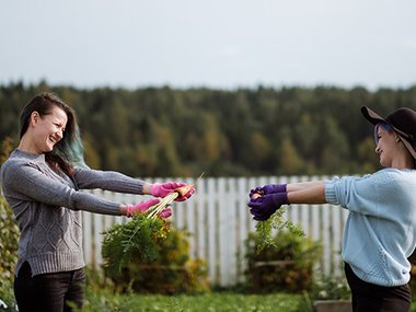Two people showing off to each other the carrots they got from their garden