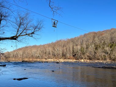 A man suspended from a wire takes water samples from a wide river.