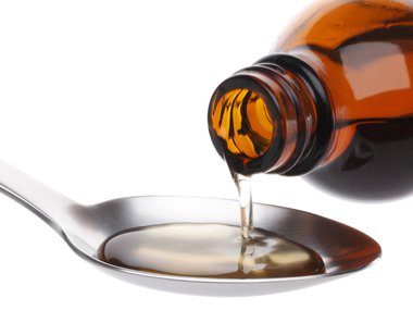 A thick yellowish liquid being poured from a brown medicine bottle into a silver spoon.