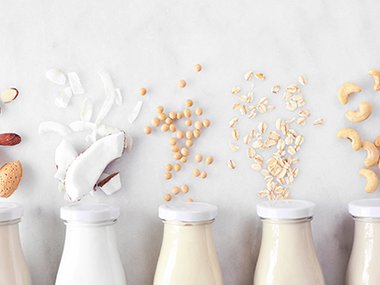 An image of glass containers with various types of plant-based milks, such as almond and coconut.