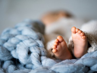 A photo of baby feet. The baby is laying on a blue blanket. The feet are in focus. The body and head are in the background out of focus.