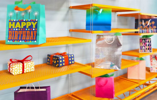 Birthday gifts in bright colored bags sitting on a vivid orange shelf in the Challenge Lab.jpg