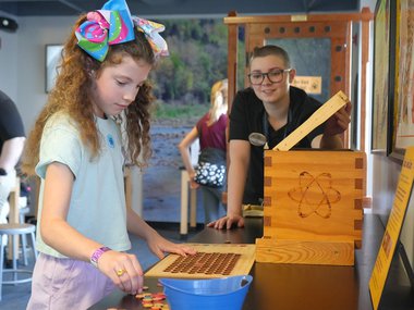 little girl wearing a large bow in her hair interacting with an activity in the Eco Lab while a staff member overlooks