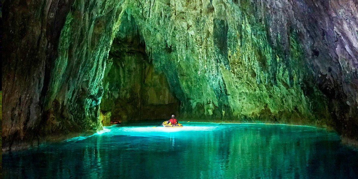Explorer navigates a raft through a beautiful green and blue cave for the Giant Screen Film Ancient Caves
