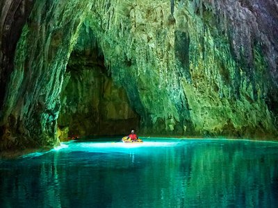 Explorer navigates a raft through a beautiful green and blue cave for the Giant Screen Film Ancient Caves