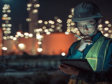 Power Plant worker is wearing a hard hat and yellow vest while reviewing information on a tablet