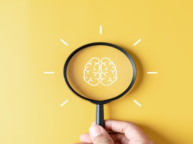Magnifying glass used to look at a illustration of a brain against a yellow background.jpg