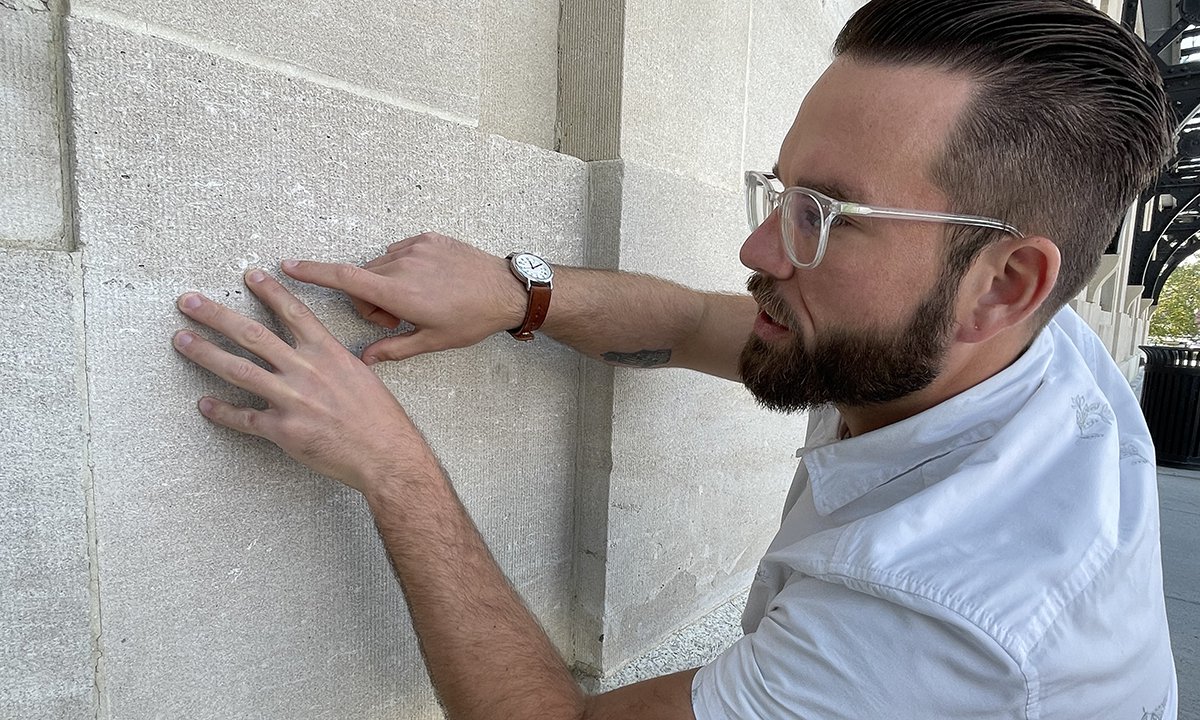 Man in white shirt wearing glasses looking at a wall and using his finger to feel for fossils.