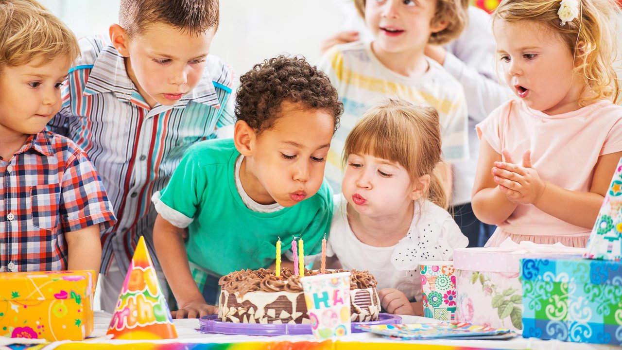 Image of a happy birthday party with gifts as two children blow out candles on a birthday cake.jpg