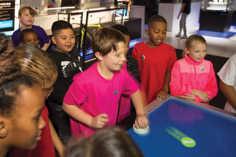 Boy playing against the air hockey robot while other children watch in the Speed exhibition.