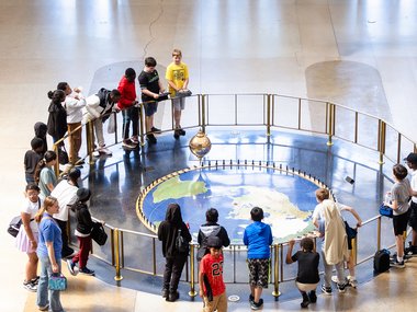 A group of students surround the Foucault Pendulum in the lobby of the Rotunda