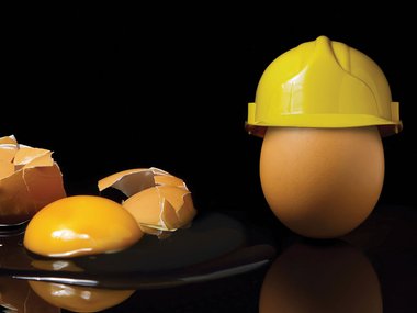 A broken egg next to an egg with a hardhat on top it.