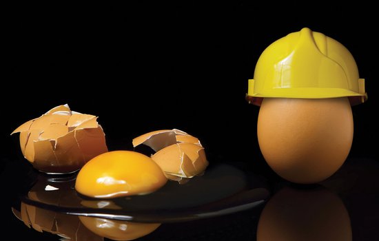 A broken egg next to an egg with a hardhat on top it.