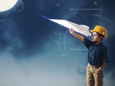 A child in a construction hat launches a large paper airplane as mathematical and scientific graphics float around him.