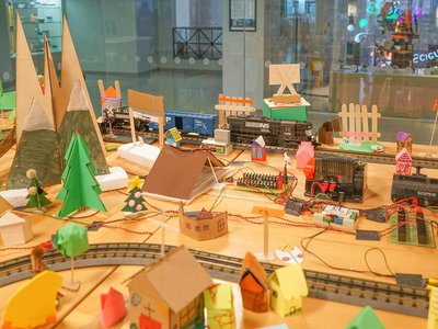 Toy train on traintracks going through colorful cardboard town. This set up is in The Forge.