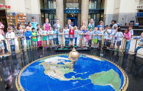 A photo of guests on a field trip at the Science Museum standing around the outside of the barrier around the pendulum.
