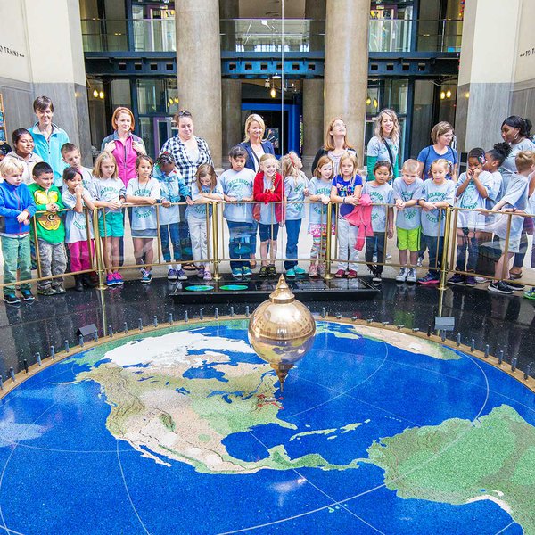 A photo of guests on a field trip at the Science Museum standing around the outside of the barrier around the pendulum.