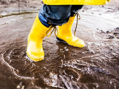 Yellow rainboots splashing in a muddy puddle.